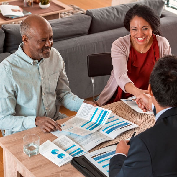 couple sitting at kitchen table covered in paperwork shaking hands with financial agent